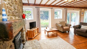 Una sala de estar acogedora con chimenea de piedra, muebles de madera y ventanas grandes que ofrecen vistas a la vegetación.
