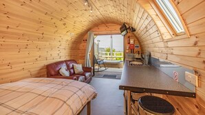 Interior acogedor de una cabaña de madera, con cama, sofá, zona de comedor y vistas al exterior.