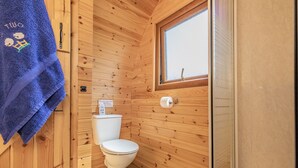 Un baño pequeño con paneles de madera, un inodoro, una ventana y una toalla colgada en la pared.