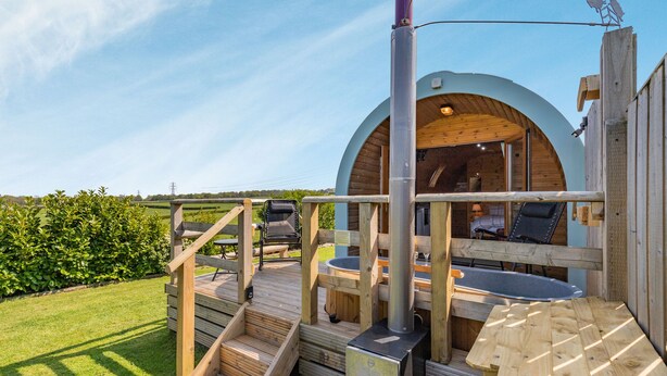 Una terraza de madera con un jacuzzi, una zona de estar cubierta y vistas del paisaje circundante.