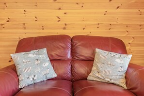 A brown leather sofa with two patterned pillows against a wooden wall. - Two Hoots (Flint)