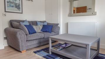 Un salon avec un canapé gris, des coussins bleus, une table basse blanche, un tapis rayé bleu et beige, un tableau encadré et un miroir au mur.