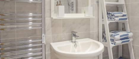 A bathroom with a white sink, a chrome towel rack, a white shelf with toiletries, and a white towel rack with towels.