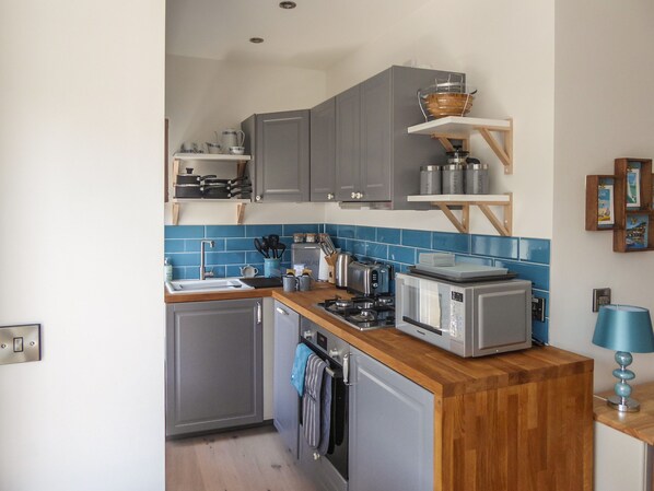 A compact kitchen with grey cabinets, a wooden countertop, a built-in oven, a microwave, and a sink. - Harbour View Apartment (Looe)