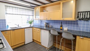 A kitchen with wooden cabinets, a black countertop, a dishwasher, a sink, and a window with a view. - End Cottage (Ashbourne)