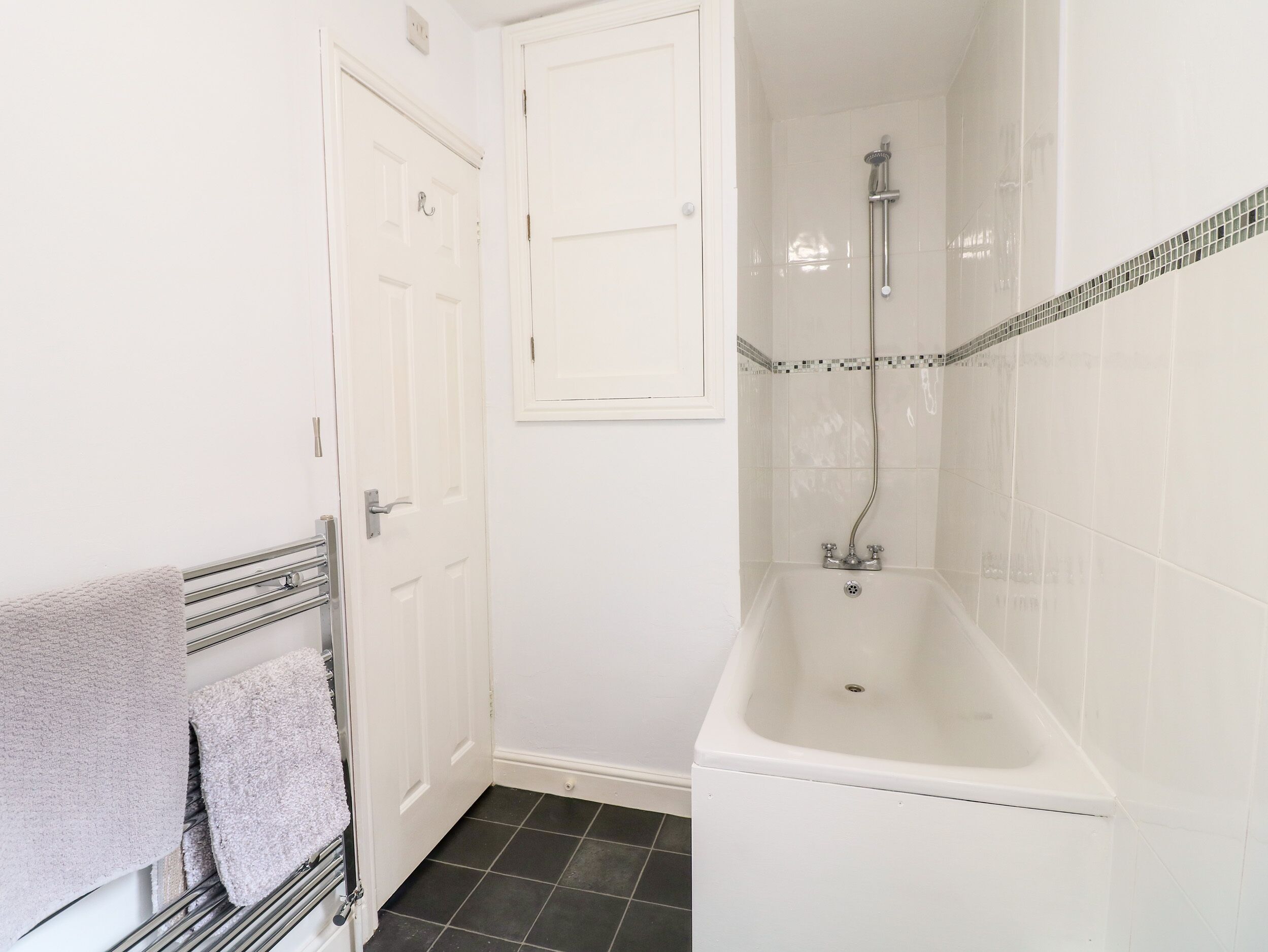 A bathroom with a white bathtub, a towel rack with towels, and a door.