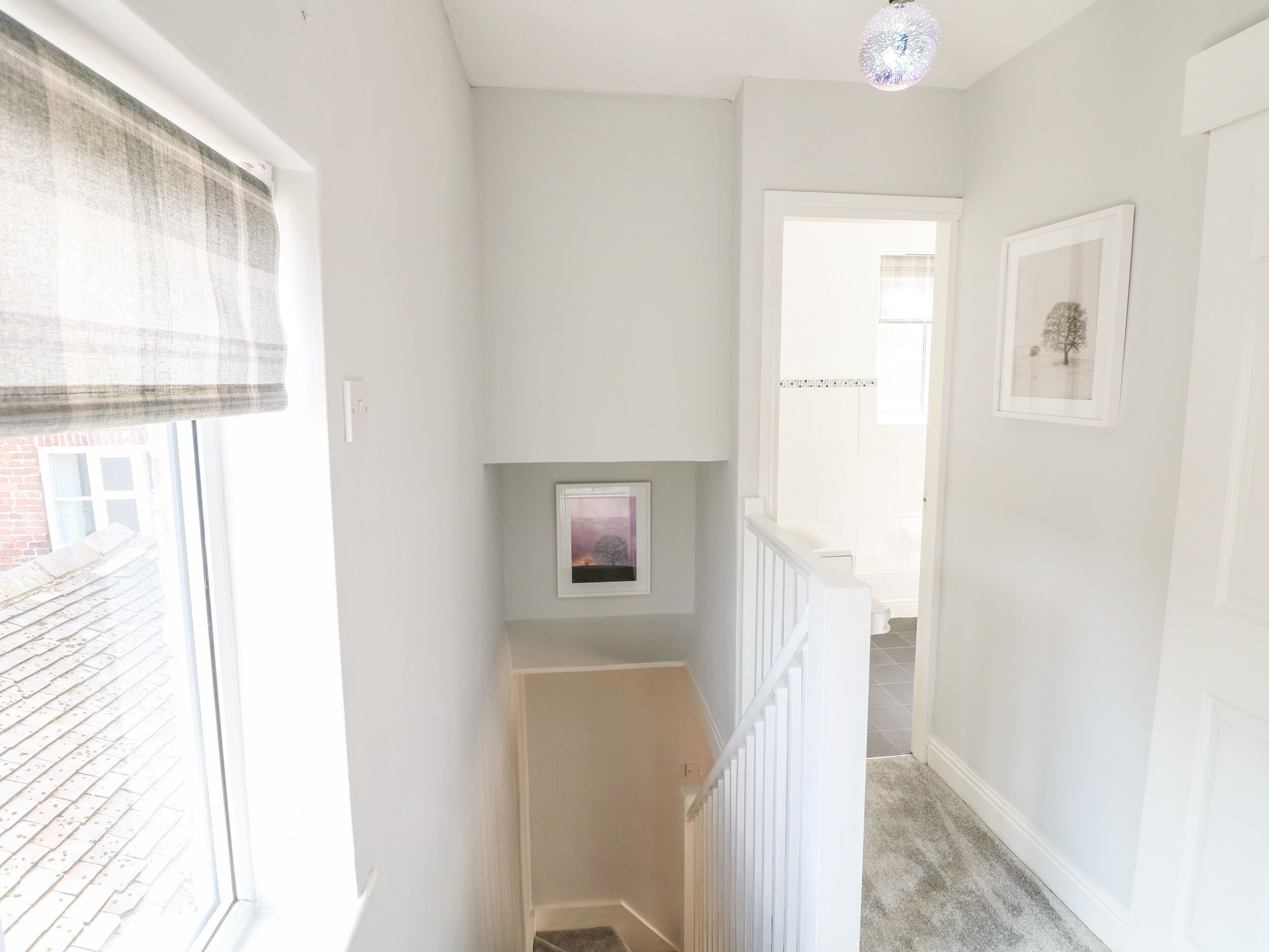 A narrow hallway with a window on the left, a picture frame on the wall, and a staircase leading to another room.