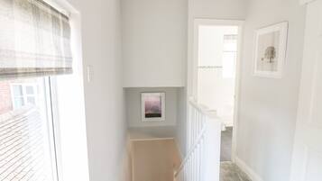 A narrow hallway with a window on the left, a picture frame on the wall, and a staircase leading to another room.
