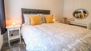 A neatly arranged bedroom with a bed, bedside table, and a mirror. - End Cottage (Ashbourne)