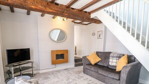 A living room with a grey sofa, a plaid armchair, a flat-screen TV, a wooden picture frame, and a staircase. - End Cottage (Ashbourne)