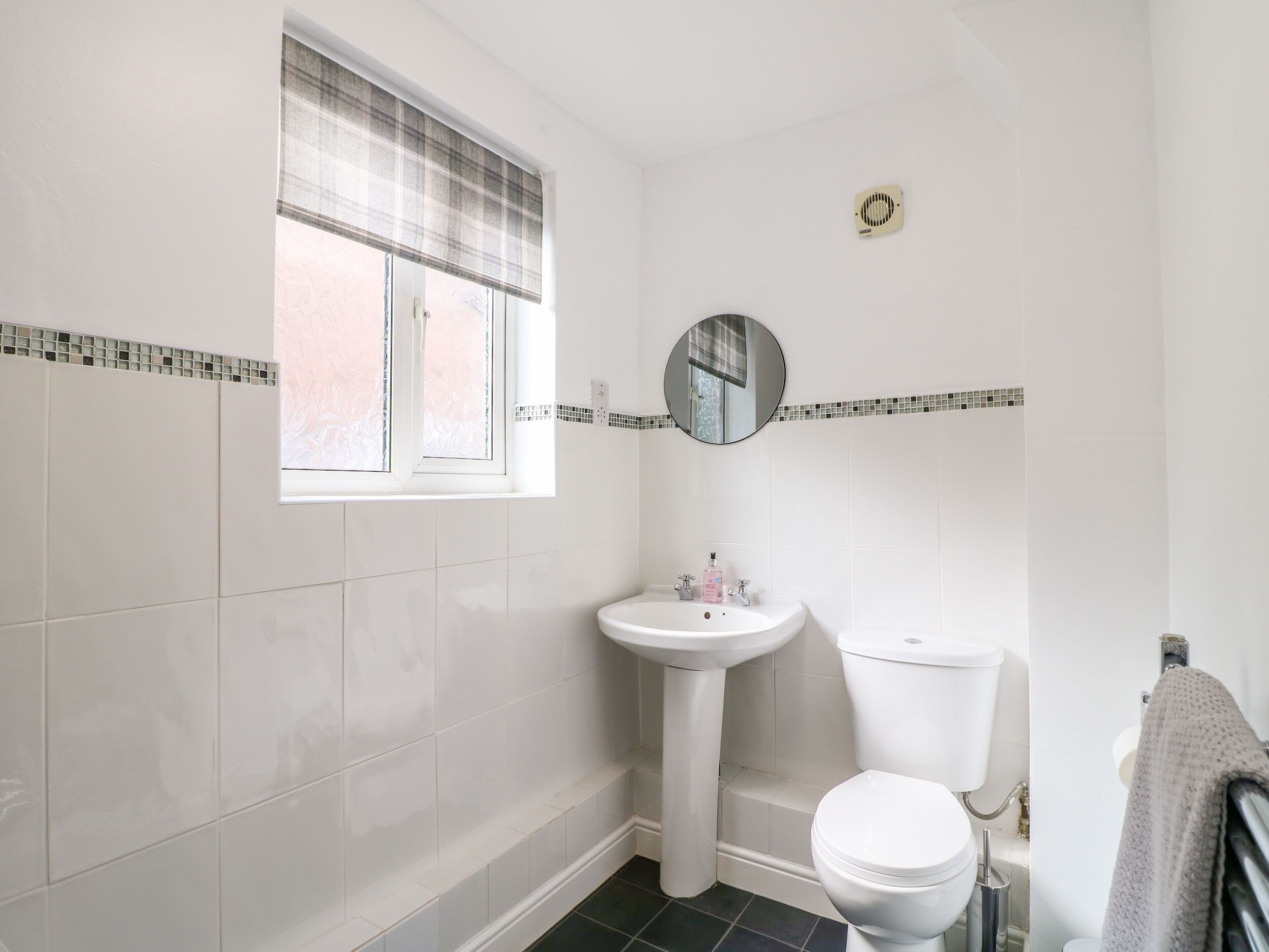Un baño con ventana, lavamanos, inodoro y espejo.