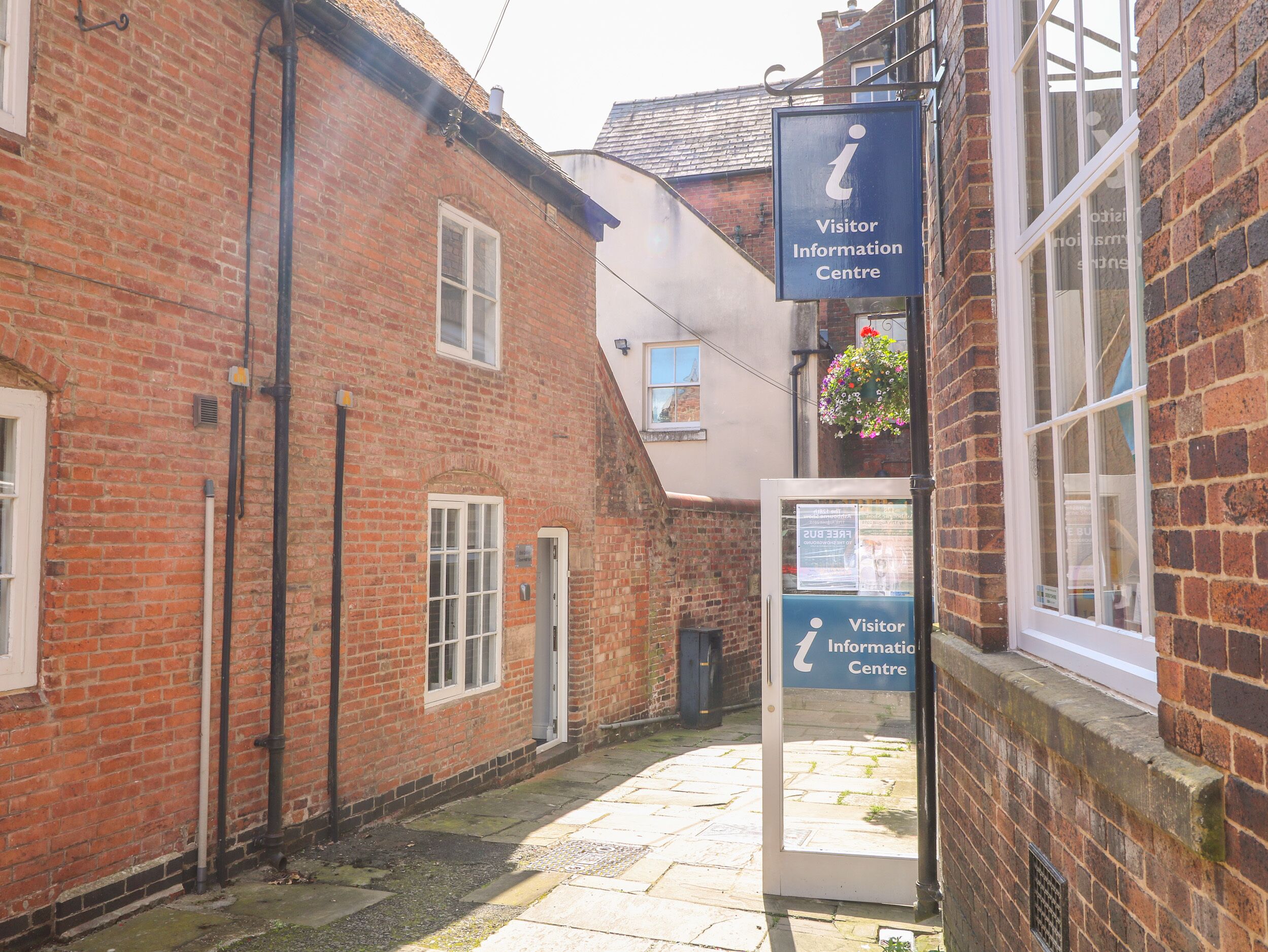 A narrow alleyway with a brick building on the left and a white building on the right. There is a sign for a Visitor Information Centre on the white building.