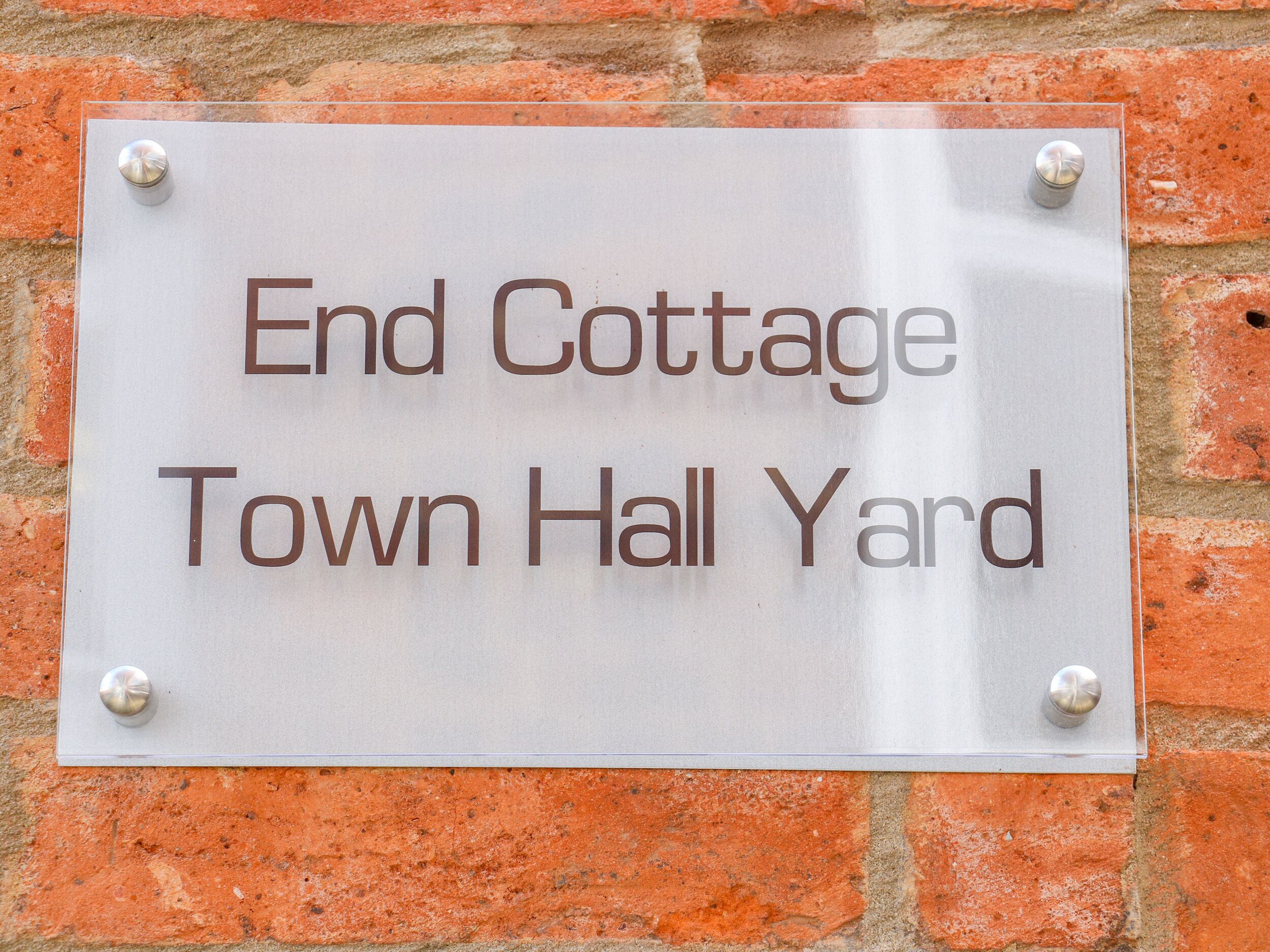Ein Schild an einer Ziegelwand mit der Aufschrift 'End Cottage Town Hall Yard'.