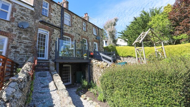 A stone house with a small front garden, a wooden swing set, and a gravel path leading to the entrance. - Bryn Teg Cottage (Menai Bridge)