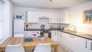 A modern kitchen with white cabinets, a wooden dining table, and two white chairs. - Bryn Teg Cottage (Menai Bridge)