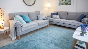 A modern living room with two grey sofas, a round mirror, a floor lamp, a blue rug, and a table with a potted plant. - Bryn Teg Cottage (Menai Bridge)