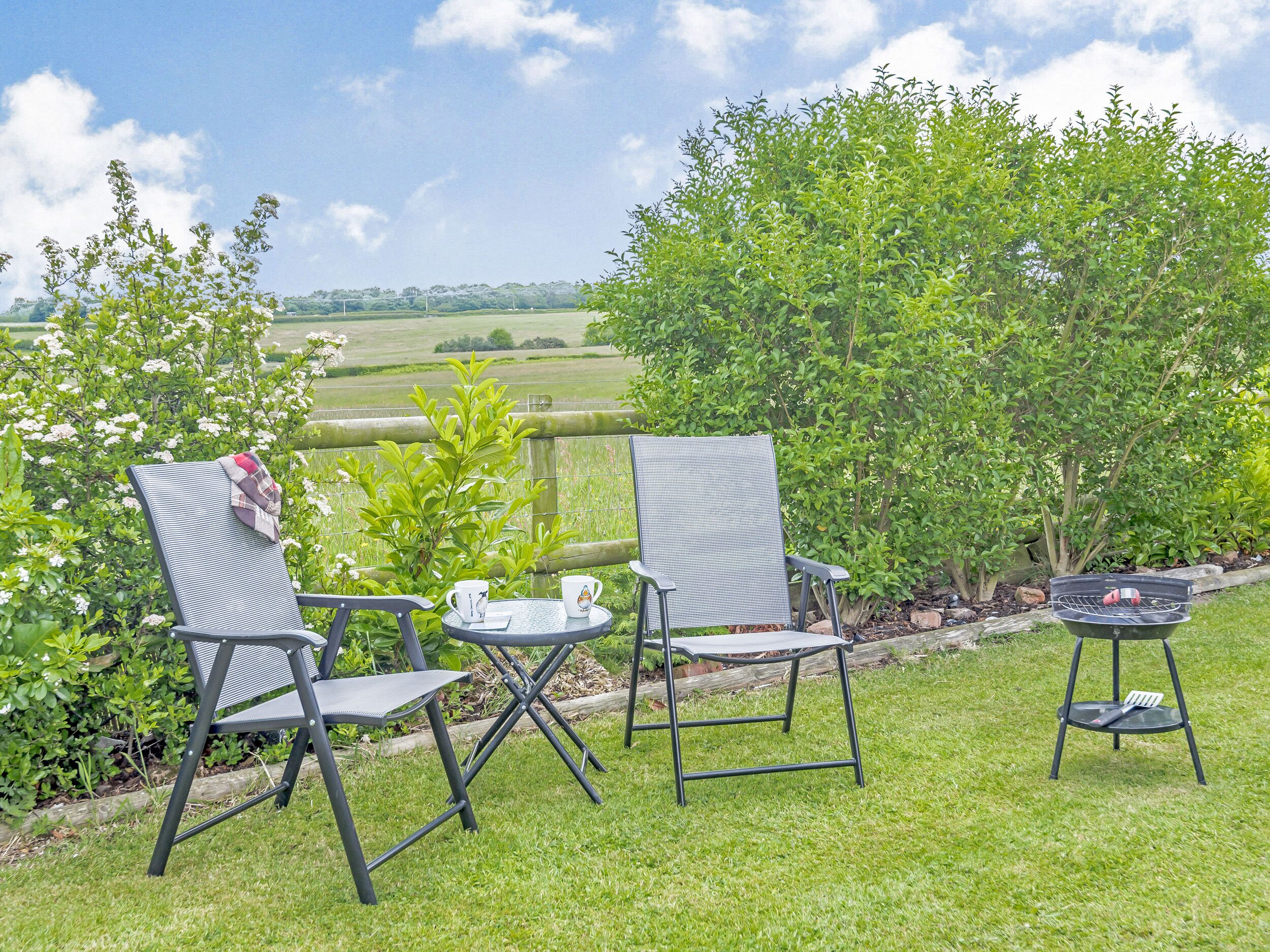 An outdoor seating area with two chairs and a table, a grill, and a view of a green landscape.
