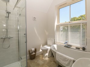 A bathroom with a glass shower enclosure, a toilet, a bathtub, and a window with blinds.