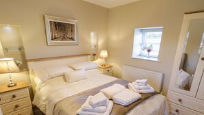 Ein ordentlich eingerichtetes Schlafzimmer mit einem großen Bett, Nachttischlampen, einem Nachttisch mit einer Vase, einem Fenster mit Ausblick und einem Spiegel.