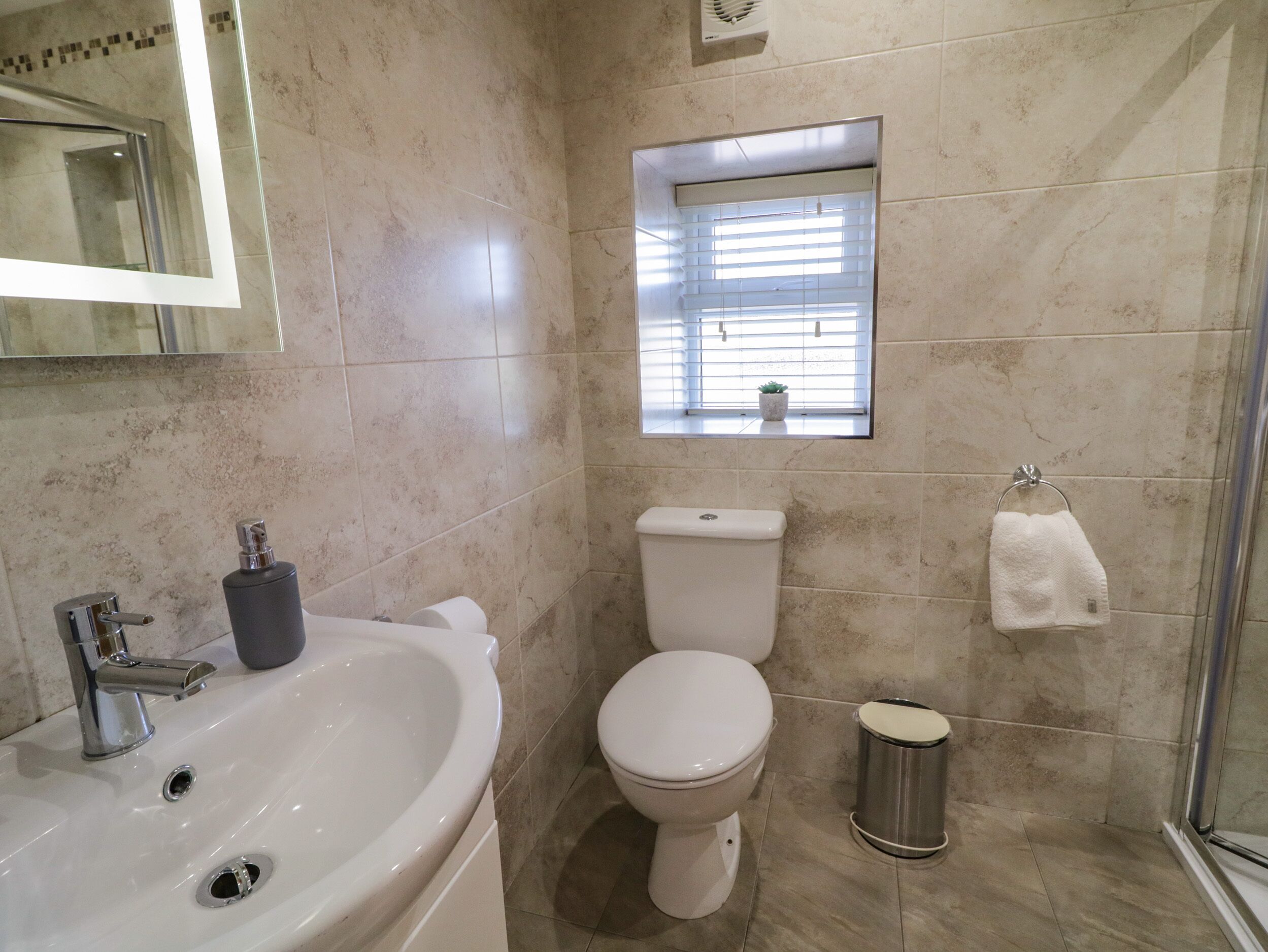A bathroom with a sink, toilet, and a small window with blinds.