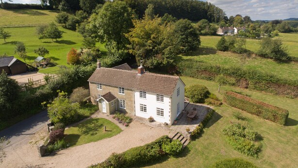 A white house with a tiled roof, surrounded by a well-maintained lawn and garden, with a clear view of the surrounding countryside. - Church View (Salisbury)