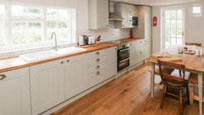 A modern kitchen with white cabinets, a wooden countertop, and a dining area with a wooden table and chairs. - Church View (Salisbury)