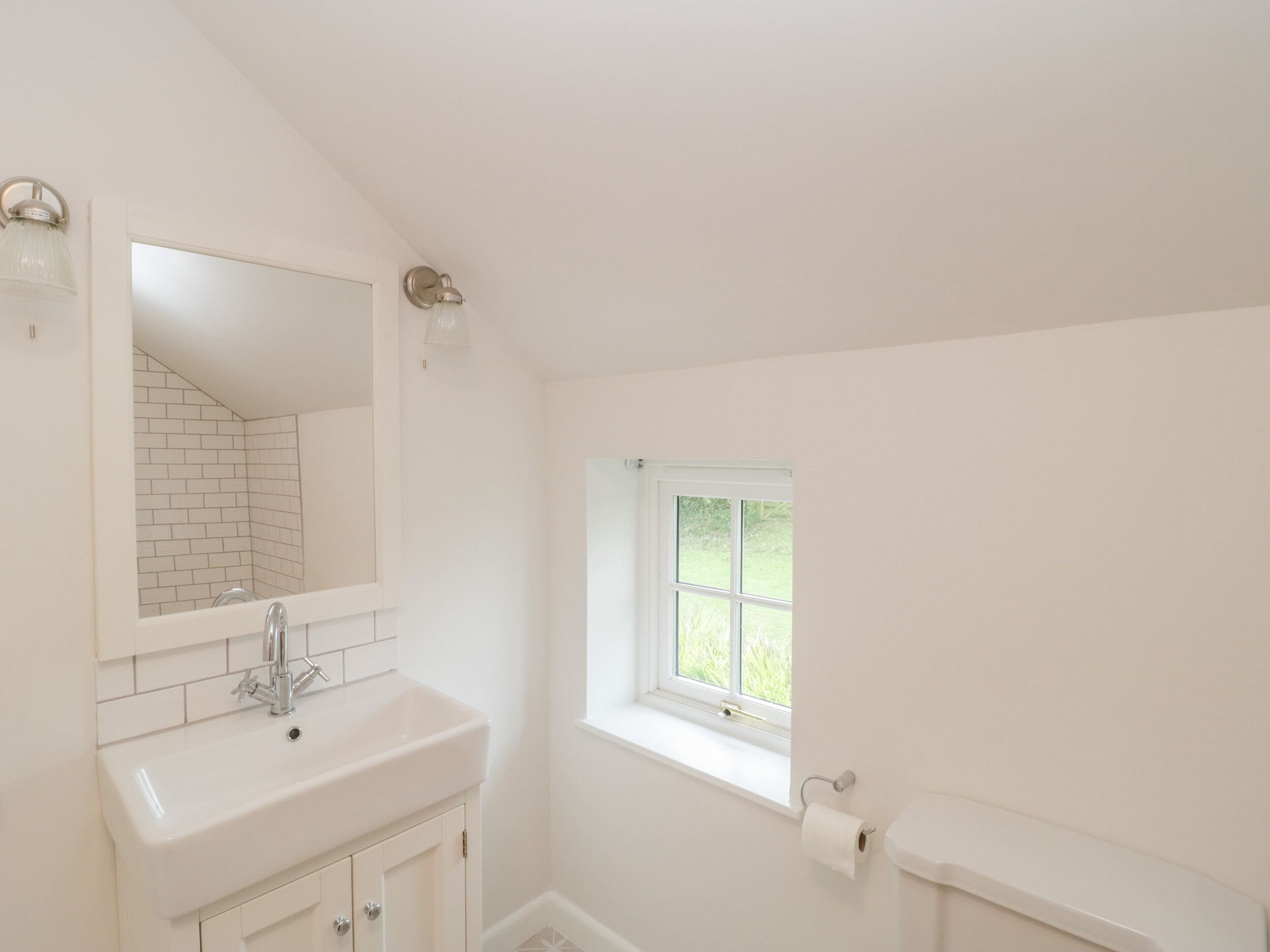 A bathroom with a white sink, a mirror, a window, and a toilet.