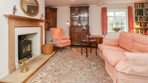 A cozy living room with a fireplace, a pink armchair, a sofa, a wooden cabinet, and a bookshelf. - Church View (Salisbury)
