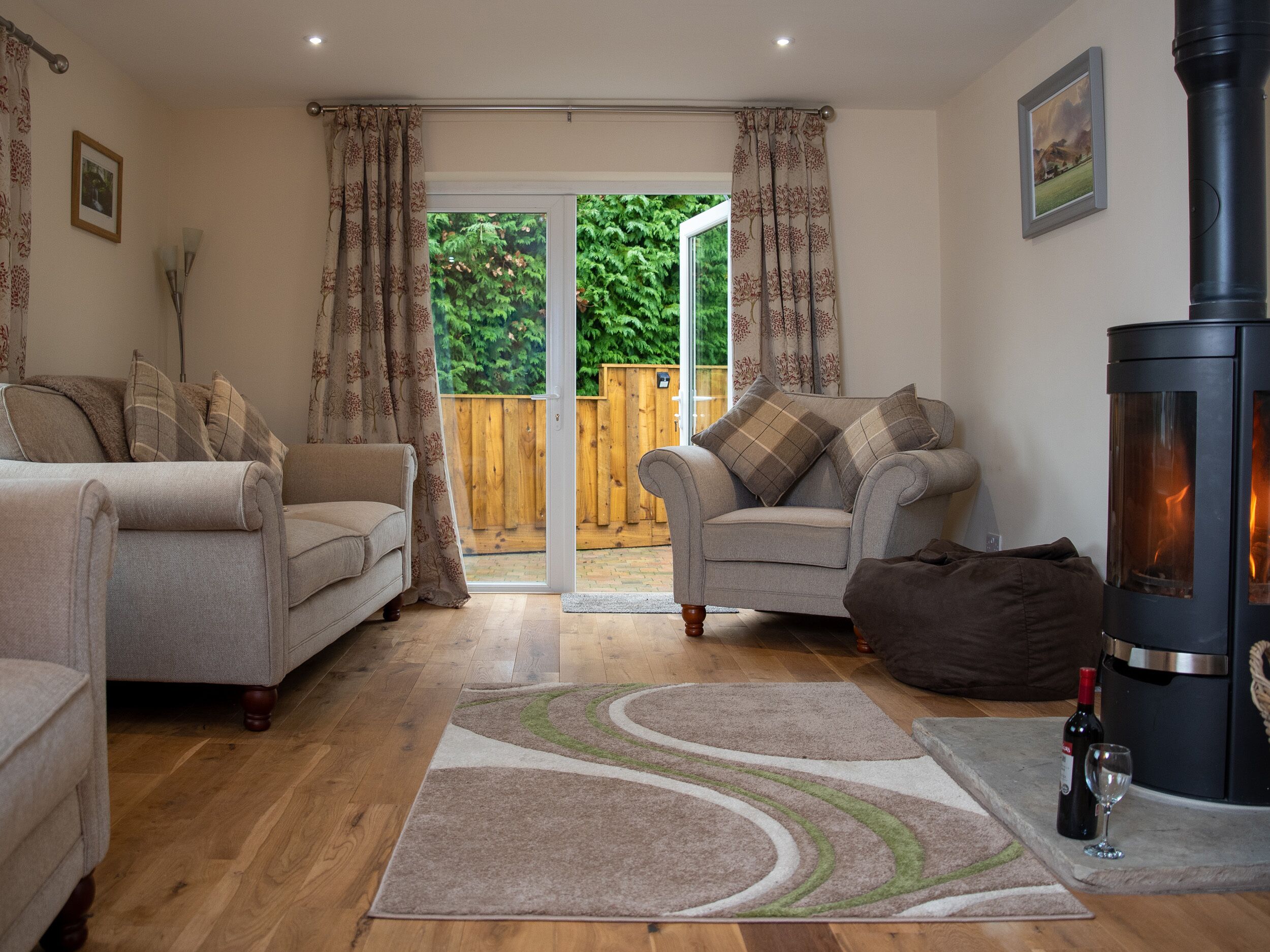 A cozy living room with two sofas, a rug, a fireplace, and a glass door leading to a garden.