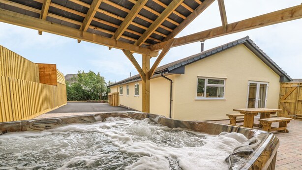 A hot tub area with a wooden pergola overhead, a picnic table, and a house in the background. - New Peny (Llandrindod Wells)