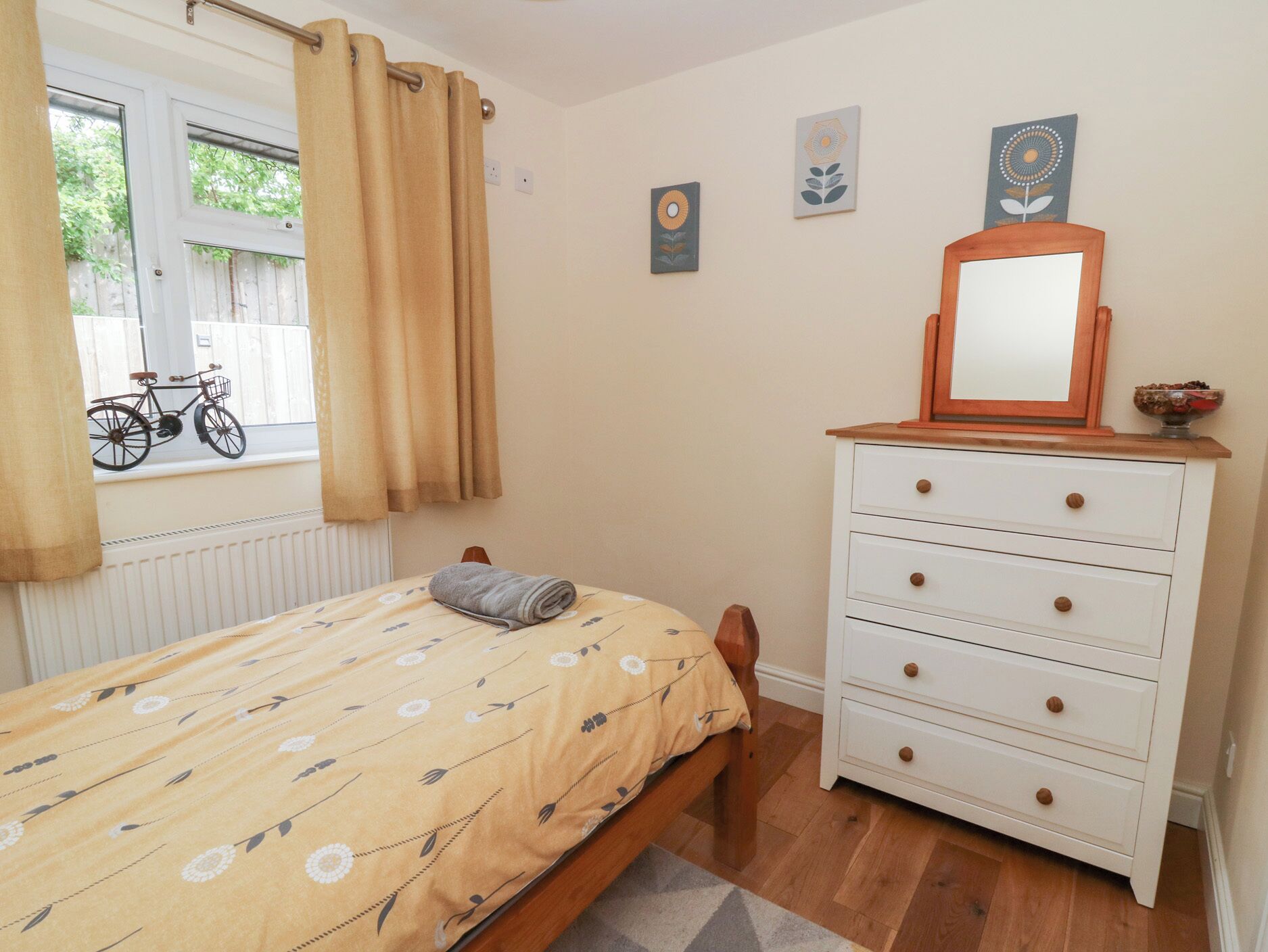 A bedroom with a bed, a dresser, a window with curtains, and a bicycle outside.