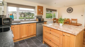 A modern kitchen with wooden cabinets, a built-in dishwasher, a granite countertop, and a window providing a view of the outdoors. - New Peny (Llandrindod Wells)