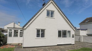 Une maison blanche à deux étages, avec un toit à pignon, une porte d’entrée et un garage.