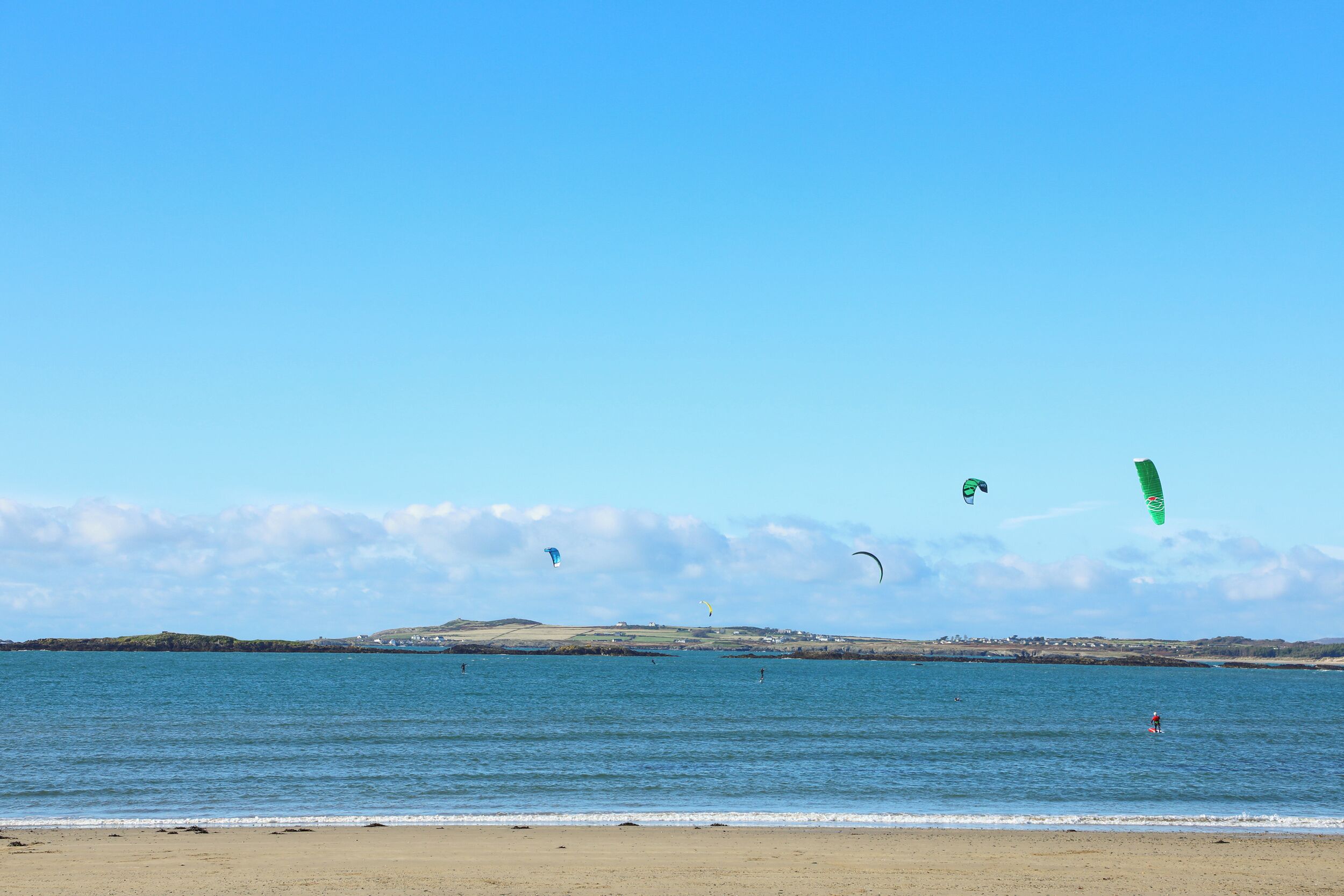 Una playa con cielo despejado, mar tranquilo y colinas a lo lejos.