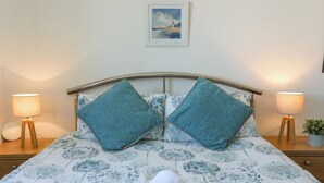 Un lit avec une couvre-lit à motifs floraux, deux coussins turquoise et un tableau encadré au-dessus.