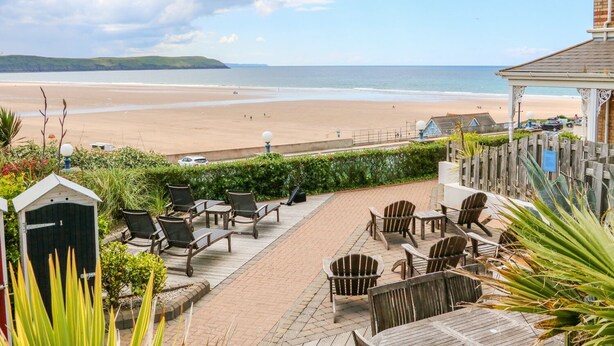 Une terrasse au bord de la plage, dotée de chaises longues et de tables, offrant une vue sur une plage de sable et la mer.