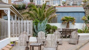 A patio area with wooden chairs and tables, surrounded by a wooden fence and various plants.