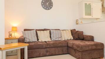 A living room with a brown sectional sofa, a wooden coffee table, a lamp, and a clock on the wall.