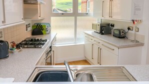 Une cuisine moderne avec des meubles blancs, une cuisinière à gaz, un évier et une fenêtre donnant sur la campagne.