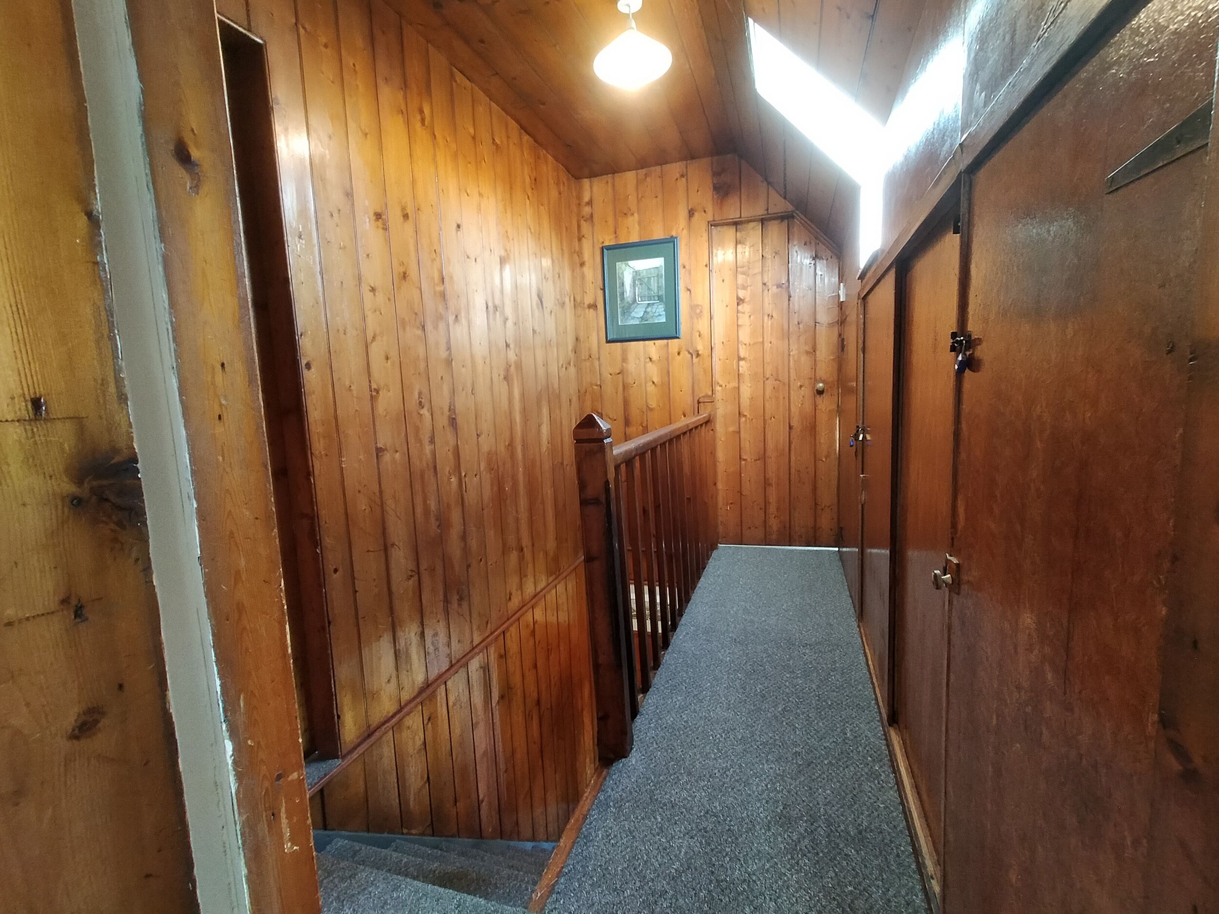 A wooden interior with a carpeted staircase, wooden walls, and a framed picture on the wall.