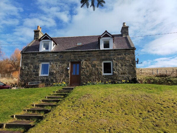 A stone house with a sloped roof, a front door, and two windows.