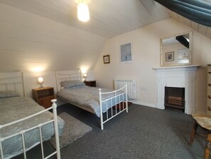 A bedroom with two single beds, a white radiator, a fireplace, and a mirror on the wall.