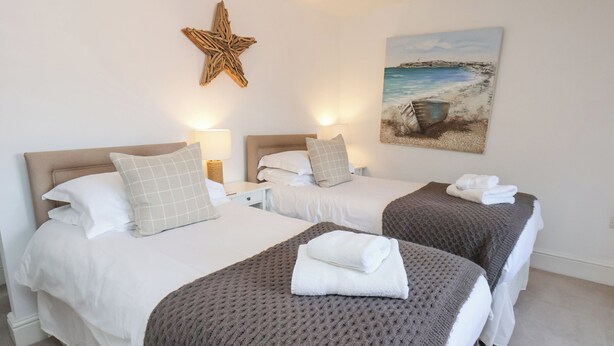 A hotel room with two beds, each with a headboard, a star decoration, and a painting of a beach scene. - Adventure Cottage (Whitby)