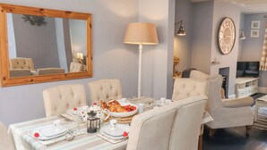 A dining area with a table set for four, a large mirror, a lamp, and a clock on the wall. - Adventure Cottage (Whitby)