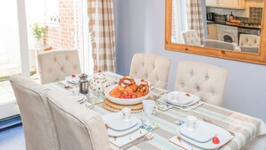 A dining area with a table set for four, including plates, cutlery, and a centerpiece of bread and fruit. - Adventure Cottage (Whitby)