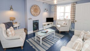 A living room with a fireplace, white sofas, a glass coffee table, and a large wall clock. - Adventure Cottage (Whitby)