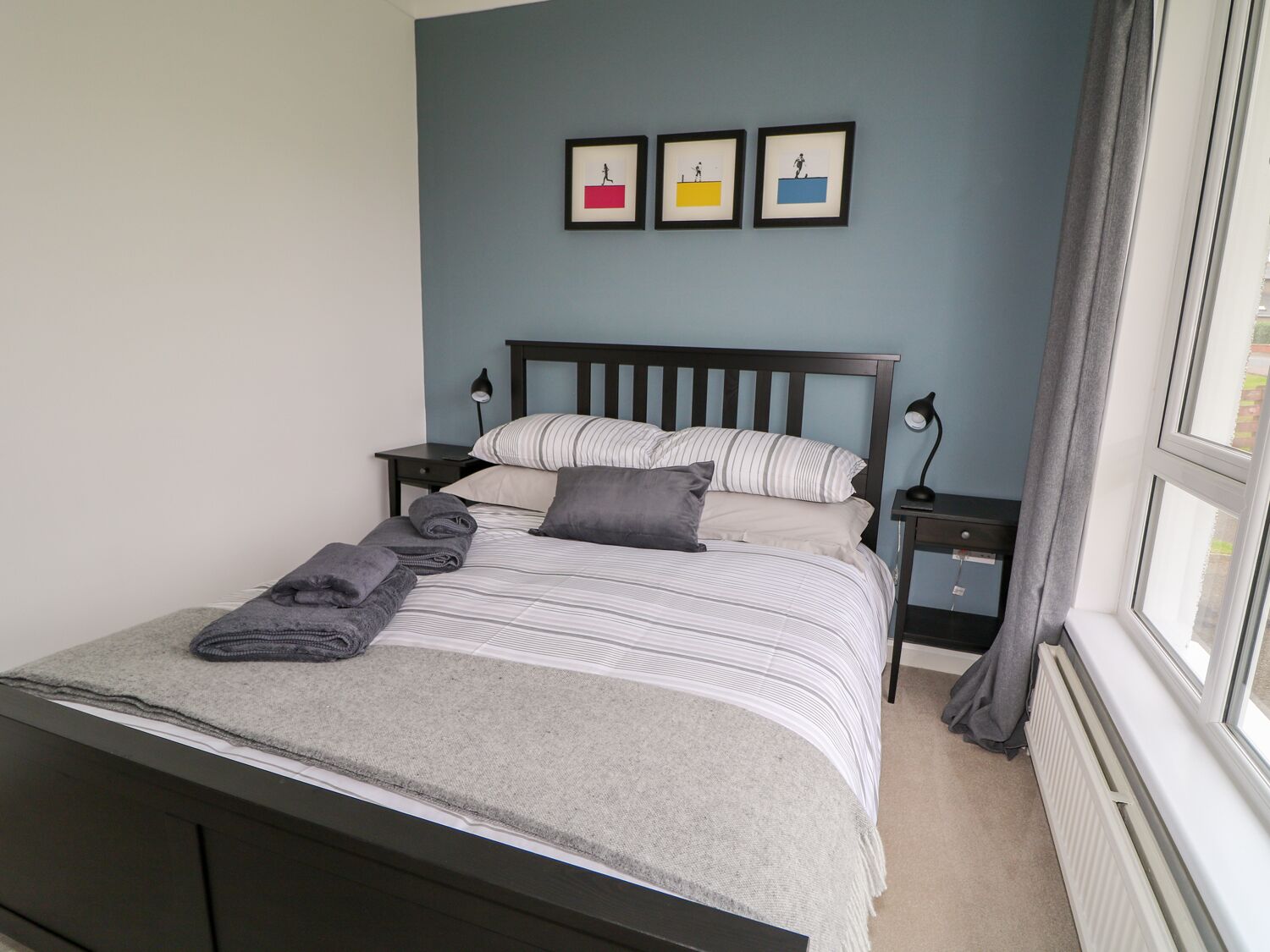 A neatly made bed with striped bedding, a gray throw blanket, and two pillows. There are two bedside tables with lamps, and a window with curtains.