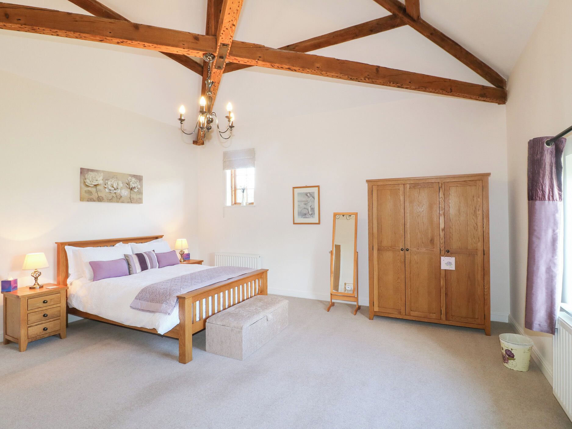 A bedroom with a wooden bed, bedside lamps, a wooden wardrobe, and a chandelier.