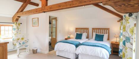 A bedroom with two beds, wooden beams, a chandelier, a desk, and a chair.