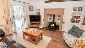A cozy living room with a fireplace, leather sofa, patterned armchair, and a television. - Willow Nook (Whitby)